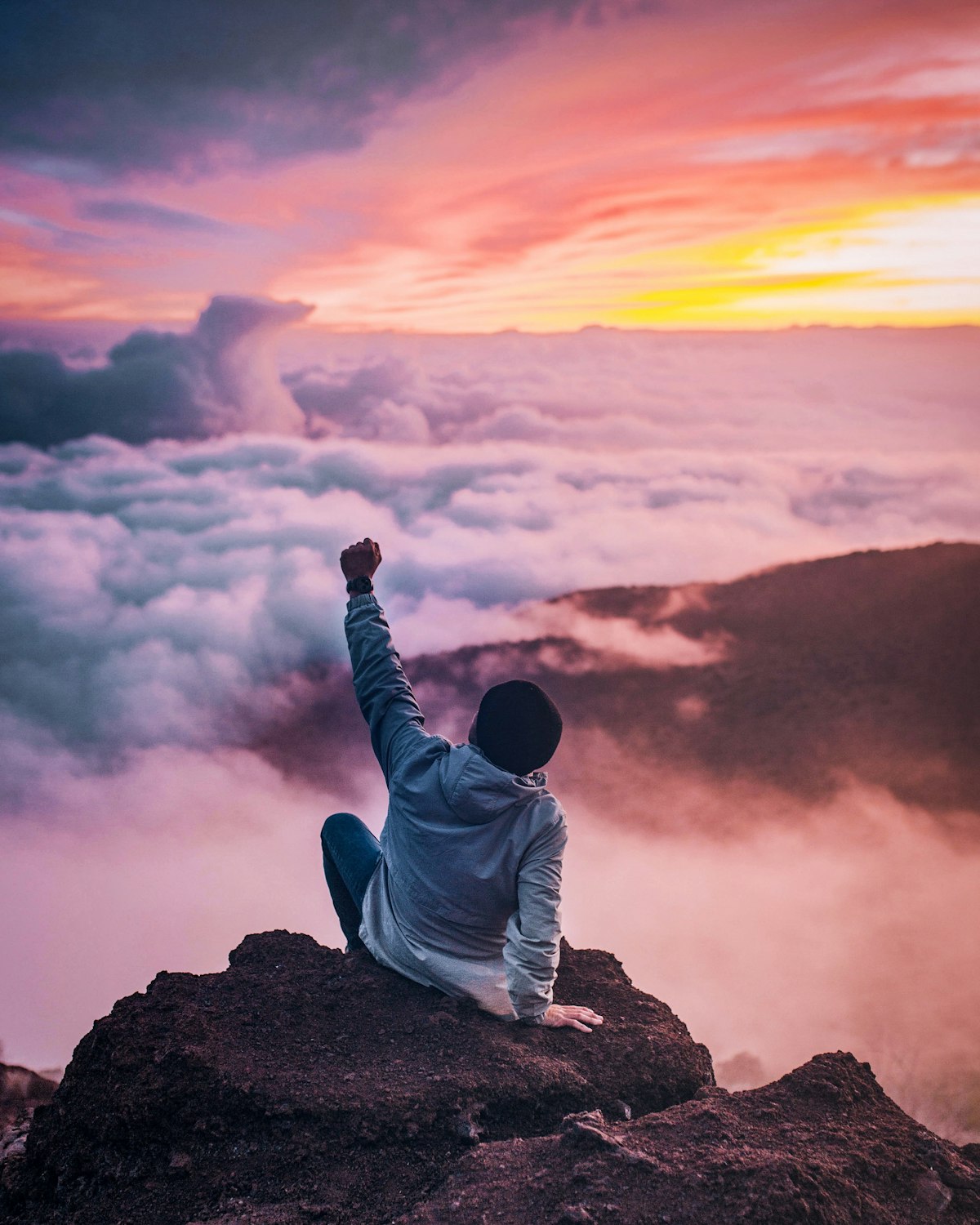 A lone figure on a mountain summit above the clouds at sunrise