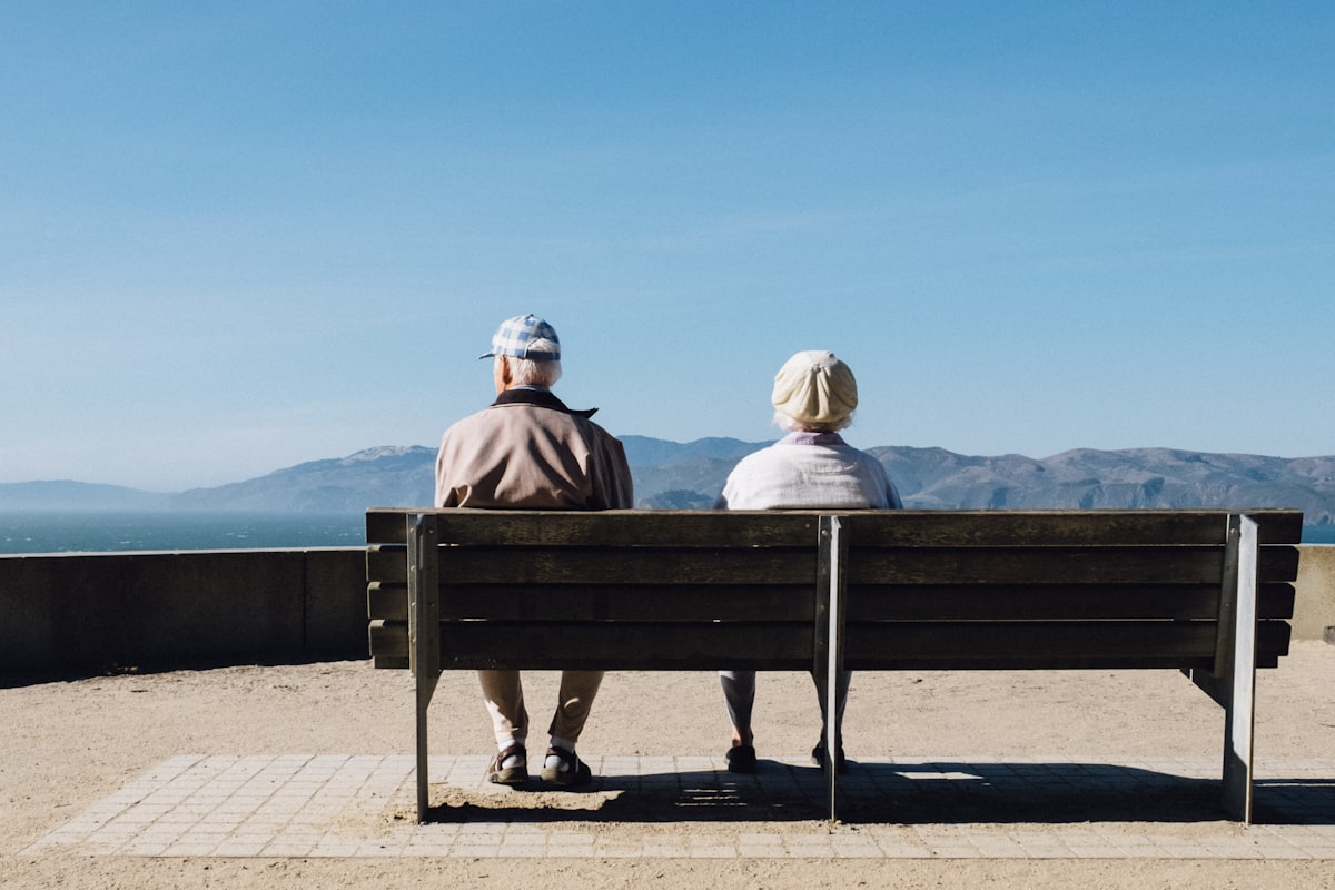 An elderly couple sitting together on a bench, looking out over the sea