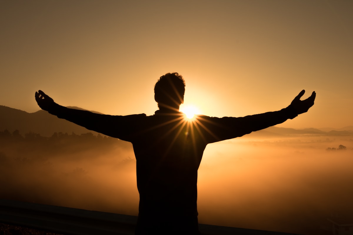 A person standing with arms open wide as the sun rises over the hills