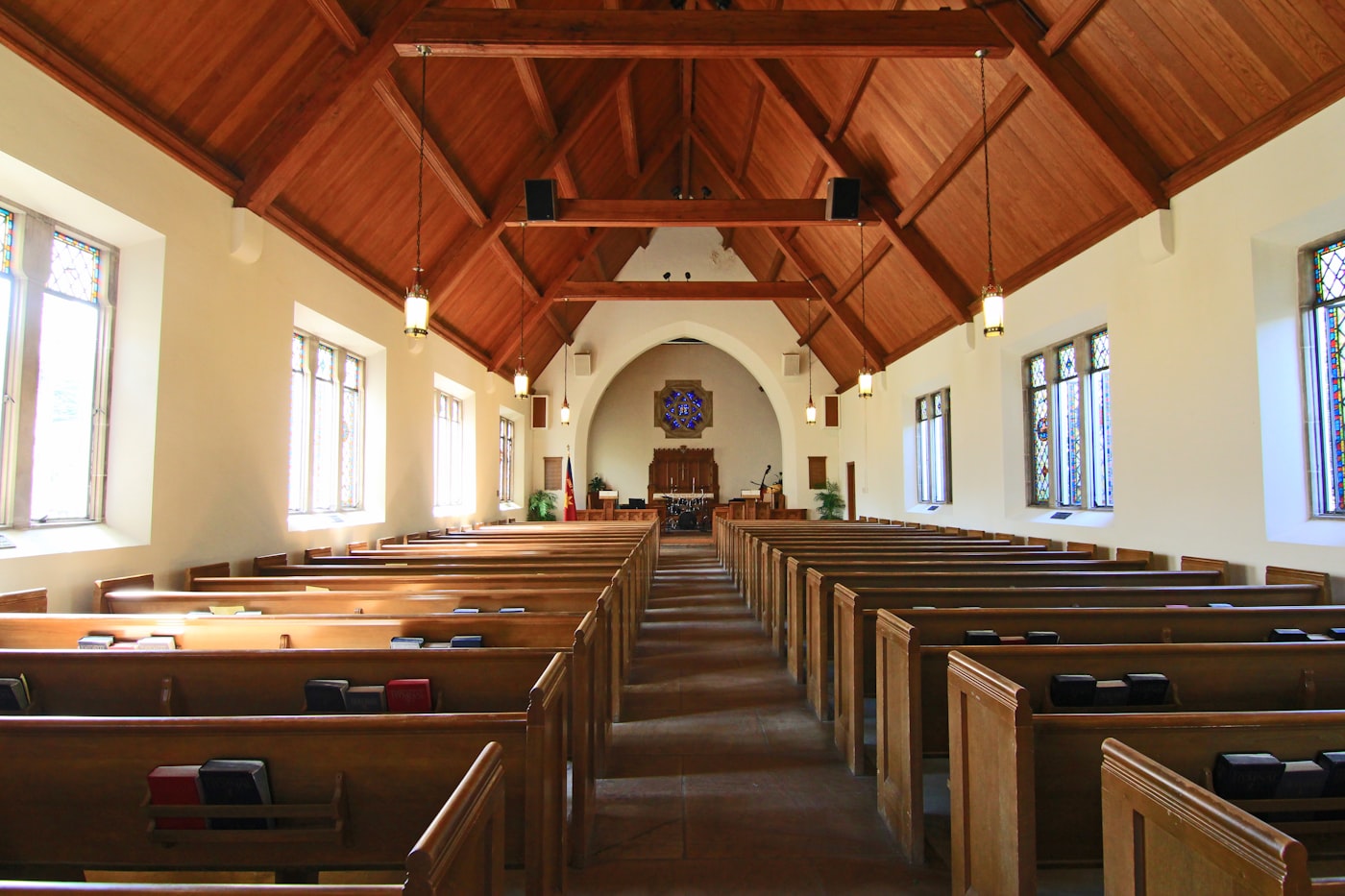 A bright church sanctuary with wooden pews and daylight through stained glass windows